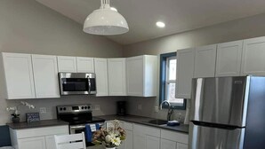 A modern kitchen with white cabinets, stainless steel appliances, a dark countertop, and a dining area with white chairs. - Castaway Cabin at Fish & Fiddle Family Resort & Extended Stay (Mountain Home)
