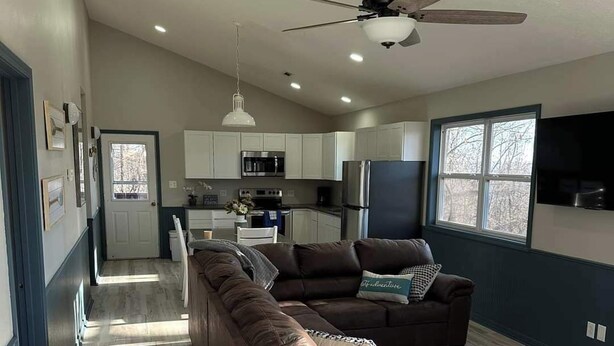 A spacious living room with a large brown sectional sofa, a ceiling fan, and a kitchen area in the background. - Castaway Cabin at Fish & Fiddle Family Resort & Extended Stay (Mountain Home)