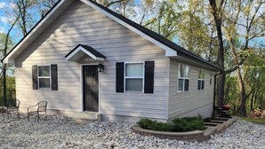A single-story house with a gabled roof, a front door, and a small porch with two chairs. - Castaway Cabin at Fish & Fiddle Family Resort & Extended Stay (Mountain Home)