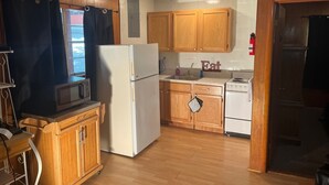 A compact kitchen with wooden cabinets, a refrigerator, a microwave, a sink, and a stove.