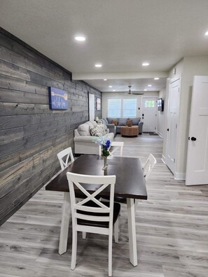 A dining area with a dark wooden table and white chairs, a gray sofa, and a small round table with a vase of flowers. - Sunset Villa at Fish & Fiddle Family Resort & Extended Stay (Mountain Home)