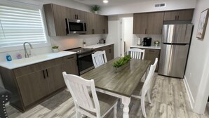 Een moderne keuken met houten kastjes, een roestvrijstalen koelkast, een magnetron en een eettafel met witte stoelen.