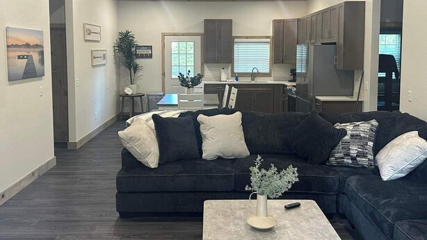 A modern living room with a dark-colored sectional sofa, a coffee table, and a dining area in the background. - Boater's Bliss at Fish & Fiddle Family Resort & Extended Stay (Mountain Home)