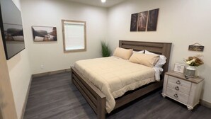 A bedroom with a bed, bedside table, and a window with blinds. - Boater's Bliss at Fish & Fiddle Family Resort & Extended Stay (Mountain Home)