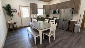 A modern kitchen with wooden cabinets, a stainless steel refrigerator, and a dining area with a table and chairs. - Boater's Bliss at Fish & Fiddle Family Resort & Extended Stay (Mountain Home)