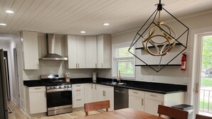 A modern kitchen with white cabinets, a black countertop, and stainless steel appliances. There is a wooden dining table with benches. - Secluded Hideaway at Fish & Fiddle Family Resort & Extended Stay (Mountain Home)