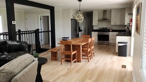 A spacious living area with a wooden dining table and chairs, a black leather sofa, and a small side table with a plant. - Secluded Hideaway at Fish & Fiddle Family Resort & Extended Stay (Mountain Home)
