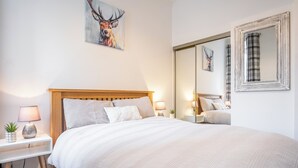 A bedroom with a large bed, two bedside tables with lamps, a mirror, and artwork on the walls.