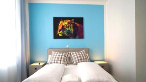 Habitación de hotel con una cama, dos mesitas de noche, una pared azul y un cuadro abstracto de colores sobre la cama.