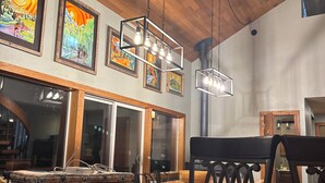 A restaurant interior with wooden tables and chairs, hanging pendant lights, and framed artwork on the walls.