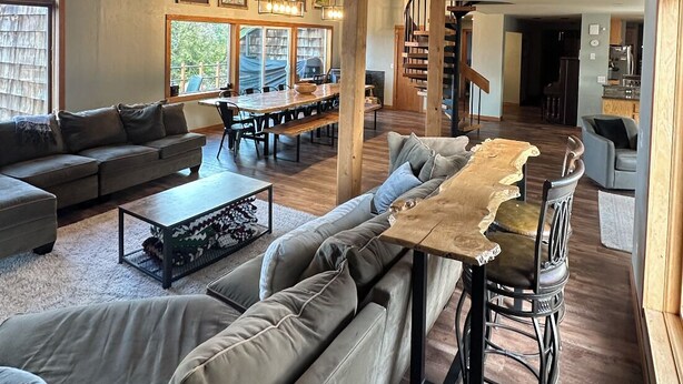 A spacious living area with a high ceiling, wooden beams, a dining table, and a staircase leading to an upper level.