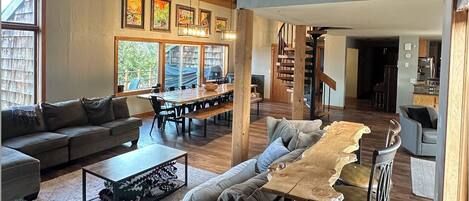 A spacious living room with a large wooden dining table, a sofa, and a staircase leading to an upper level.