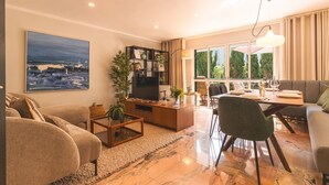 A modern living room with a sofa, coffee table, TV, and dining area. - Costa Azul by Atlantic Holiday (Funchal)