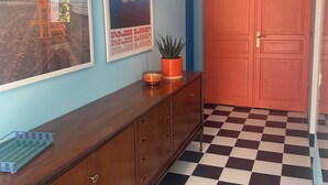 Un couloir avec un sol à carreaux, une console en bois, une plante en pot et deux tableaux encadrés accrochés au mur.