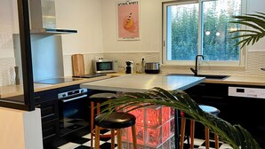 Une cuisine moderne avec un carrelage noir et blanc, une hotte en acier inoxydable, un four à micro-ondes, un évier et un tabouret de bar agrémenté d’un élément décoratif en verre.