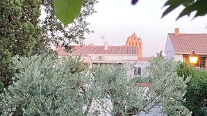 Une cour plantée d’oliviers, un bâtiment surmonté d’un toit de tuiles rouges et un clocher.