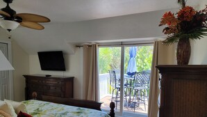A bedroom with a bed, a dresser, a TV, and a balcony with outdoor furniture.