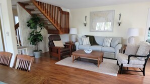 A living room with a wooden staircase, a sofa set, a coffee table, and a dining area with a table and chairs.