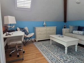 A room with a desk, chair, dresser, and a sofa.