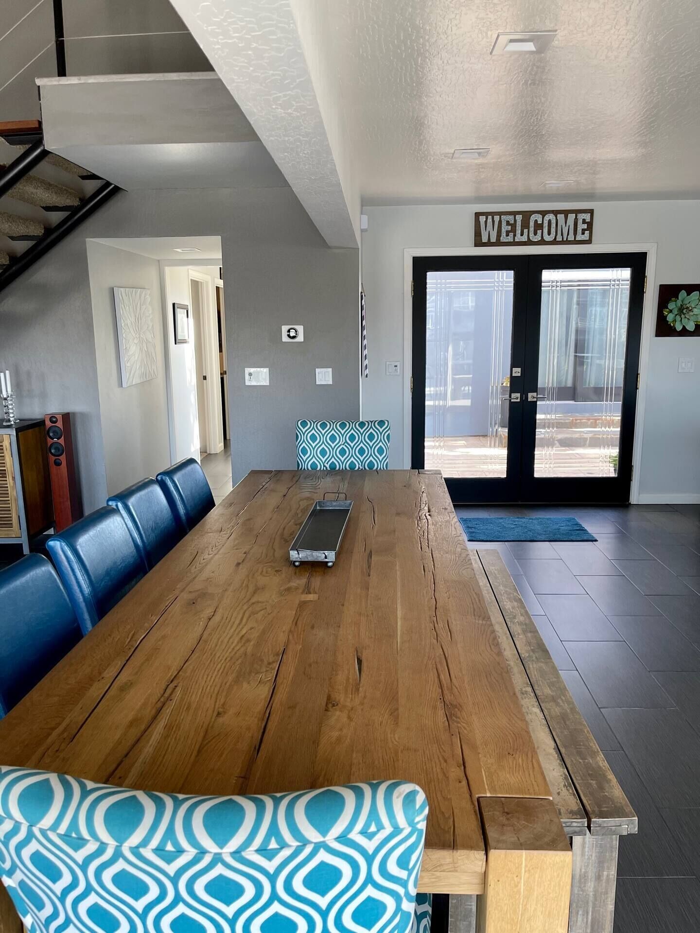 A spacious room with a wooden dining table, blue patterned bench, and a 'WELCOME' sign above the door.