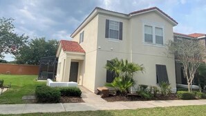 A two-story house with a red-tiled roof, a covered patio, and a well-maintained lawn. - Peaceful 4 Bedroom Townhome (Kissimmee)