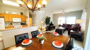 A modern kitchen with wooden cabinets, a dining area with a wooden table set for four, and a living room with a sofa and a TV. - Peaceful 4 Bedroom Townhome (Kissimmee)