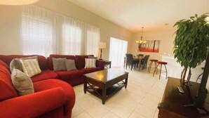 A living room with a red sofa set, a wooden coffee table, and a dining area with a table and chairs. - Peaceful 4 Bedroom Townhome (Kissimmee)