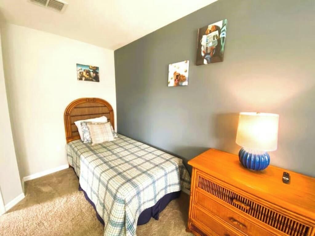 Un dormitorio con cama, cómoda, lámpara y decoración en la pared.