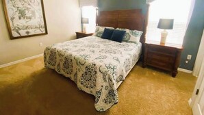 A bedroom with a large bed, a ceiling fan, a nightstand, a lamp, and a window with curtains. - Peaceful 4 Bedroom Townhome (Kissimmee)