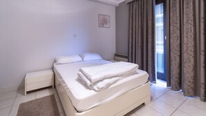 A bedroom with a bed, nightstand, and a view through a window with curtains.