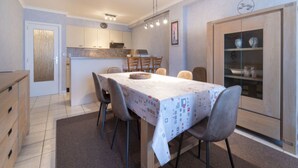 A compact kitchen with a dining area, featuring a table with a patterned tablecloth, chairs, and a cabinet with decorative items.