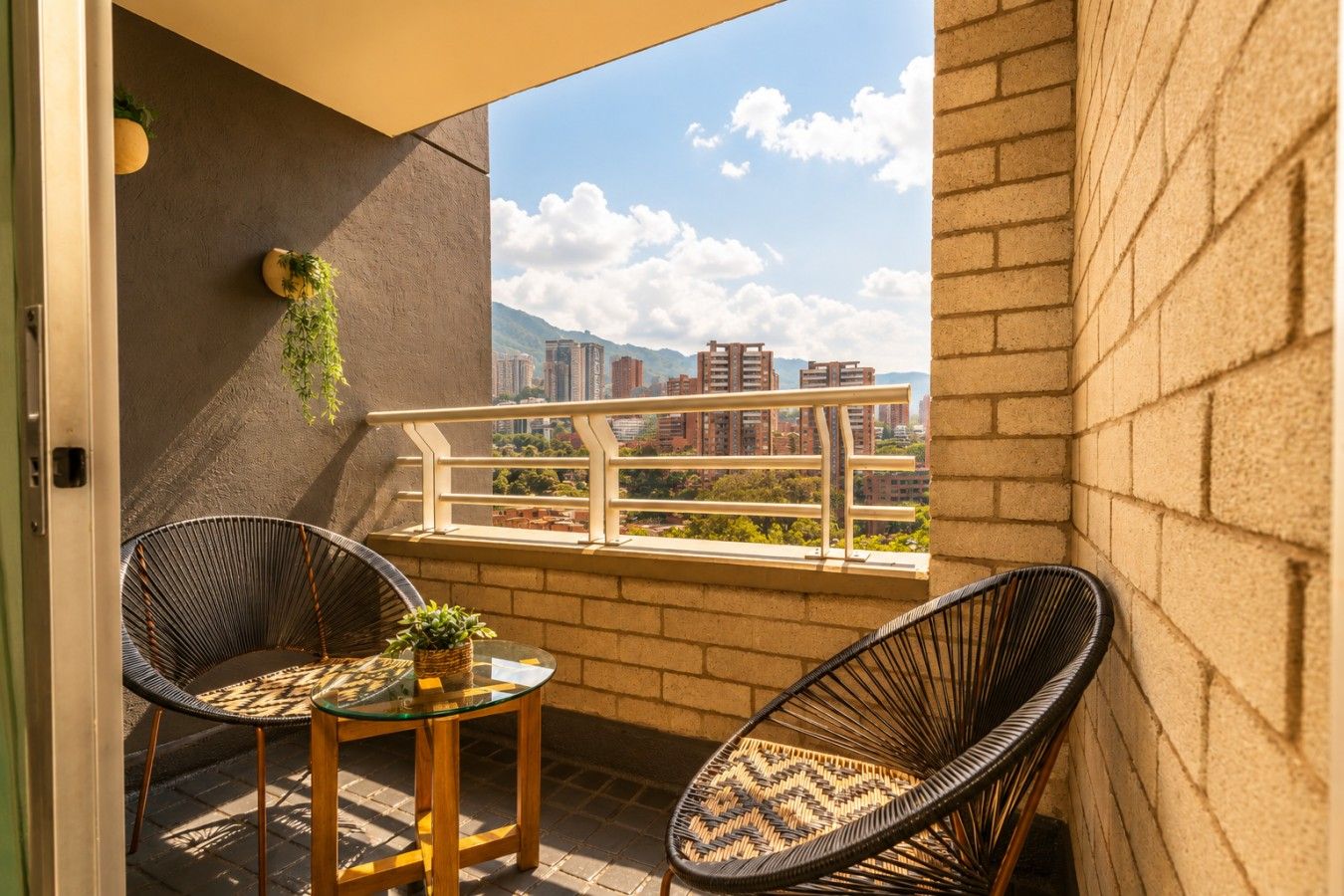A balcony with two wicker chairs, a small table, and a potted plant.