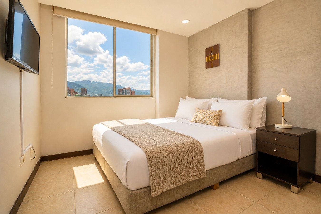 Une chambre d’hôtel avec un lit, une table de chevet, une lampe, une télévision et une fenêtre donnant sur la montagne.