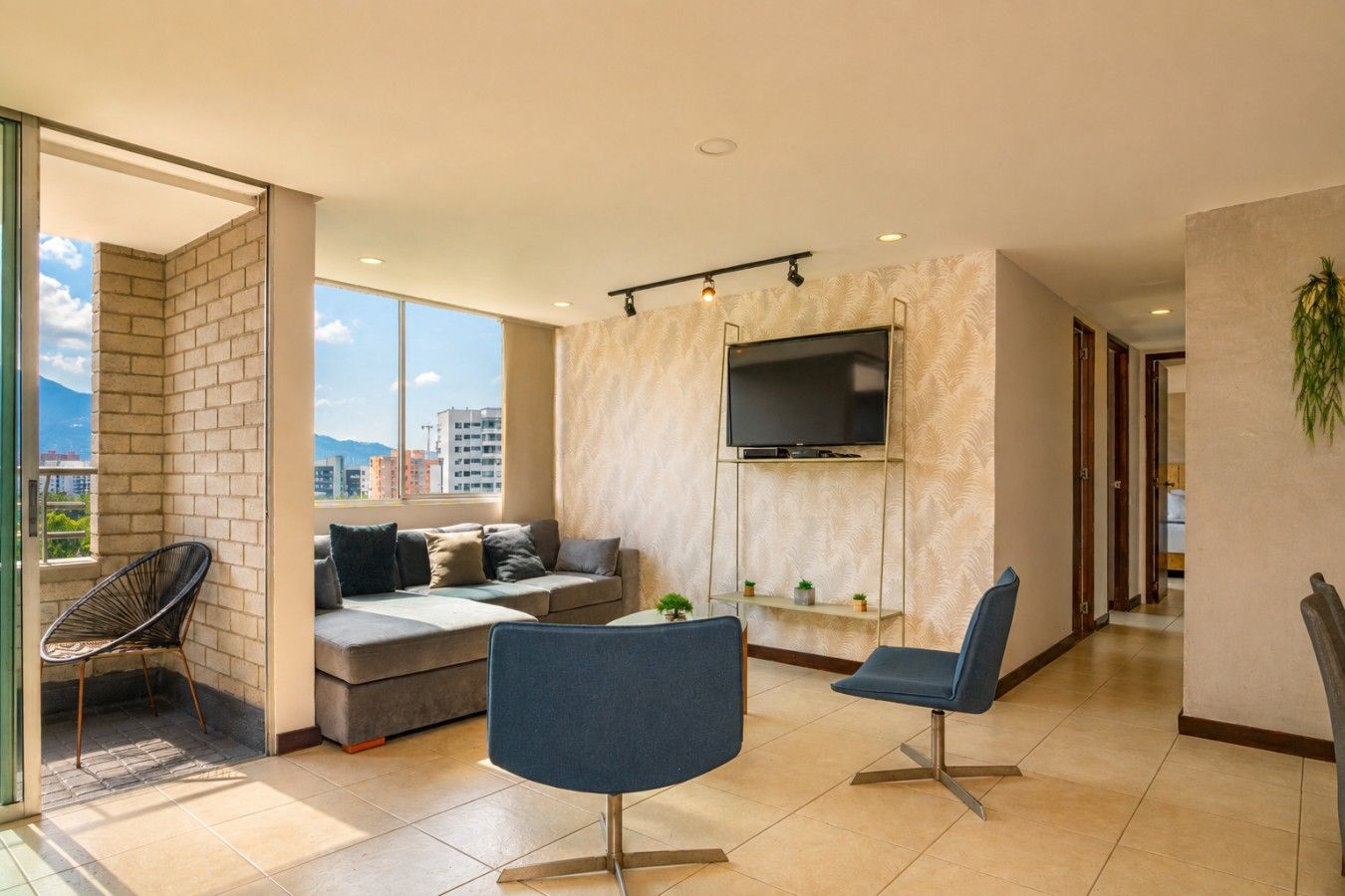 Ein modernes Wohnzimmer mit einer Couch, zwei Sesseln, einem Fernseher und einem Balkon mit einem Sessel.