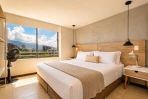 Una moderna camera d'albergo con un grande letto, un comodino, una lampada da notte, una lampada da terra e vista sulla città attraverso un'ampia finestra.