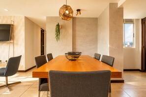 A modern meeting room with a wooden table, six chairs, a hanging light fixture, and a large window.