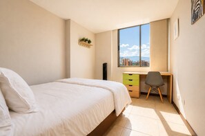Una camera da letto con un letto, una scrivania e una sedia. Si vede una finestra con vista sugli edifici.