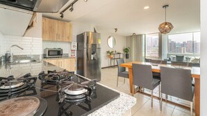 A modern kitchen with a gas stove, stainless steel refrigerator, and a dining area with a wooden table and chairs. - Penthouse Apt Poblado, City View, Rooftop Jacuzzis (Medellín)