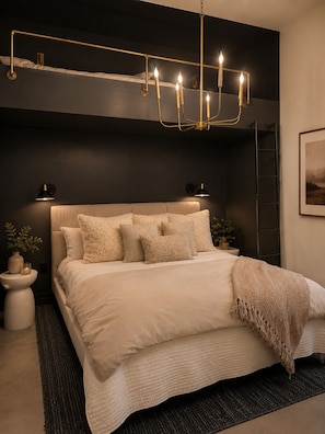 Un dormitorio moderno con una cama grande, lámparas de noche, un candelabro y una escalera apoyada en la pared.