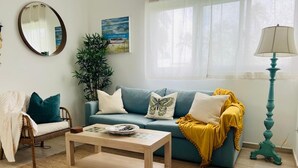 Ein Wohnzimmer mit einer Couch, einem Couchtisch, einem Sessel, einer Lampe und einer Pflanze.