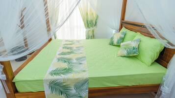 Un lit avec une couvre-lit verte et un chemin de lit orné de motifs de feuilles, une tête de lit en bois et un baldaquin en tissu blanc transparent.