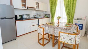 Une cuisine de taille réduite avec des meubles blancs, un réfrigérateur, un four à micro-ondes et une table avec des chaises.