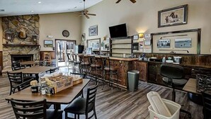 A restaurant with a stone fireplace, wooden tables, and chairs. There is a bar area with a counter and stools. - Cobbly Nob Cove #105 (Gatlinburg)