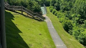 A grassy area with a pathway leading to a wooden staircase and a metal structure. - Cobbly Nob Cove #105 (Gatlinburg)