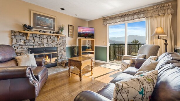 A living room with a stone fireplace, leather sofas, a wooden coffee table, and a television. - Cobbly Nob Cove #105 (Gatlinburg)