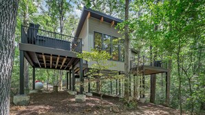 A modern treehouse with a wooden deck and glass walls, surrounded by a forest. - Treehouse - Twilight (Jonesburg)