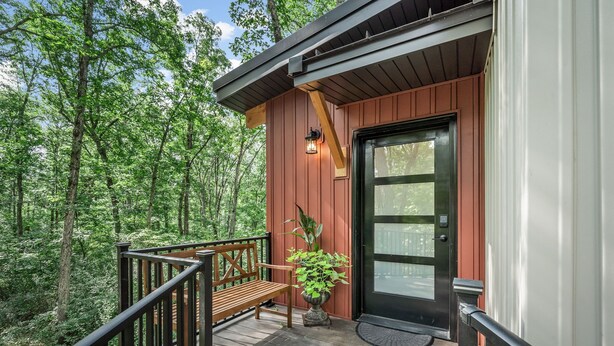 A wooden deck with a bench and a potted plant, surrounded by a forest. - Treehouse - Twilight (Jonesburg)