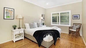 A bedroom with a bed, nightstand, lamp, chair, and window with blinds.