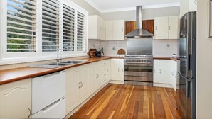 A modern kitchen with white cabinetry, stainless steel appliances, a wooden countertop, and a large window with blinds.