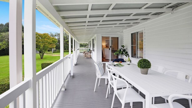 Een overdekt terras met een witte tafel en stoelen, een bloempot en uitzicht op de tuin.